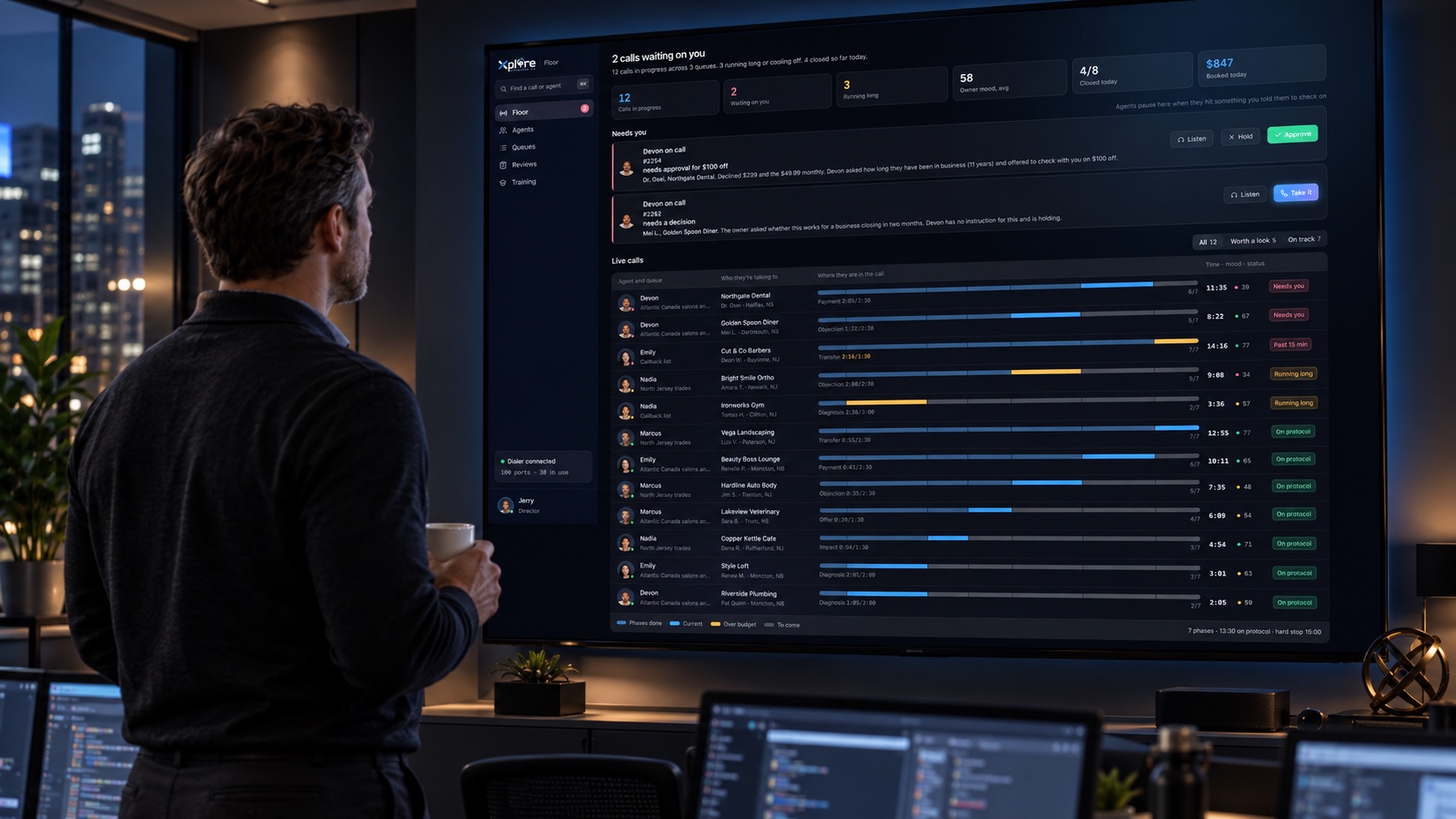 Sales operations manager with coffee reviewing the Xplore live call floor on a large wall-mounted command-center display